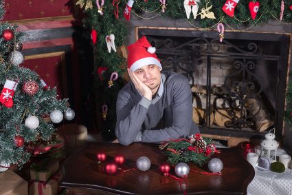 Sad young male seated with Christmas tree